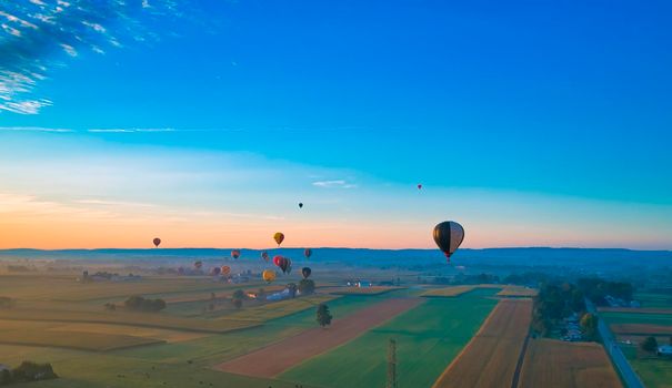 Aerial View of Many Hot Air Balloons In Flight Thru Rural Countryside On An Early Morning Balloon Festival