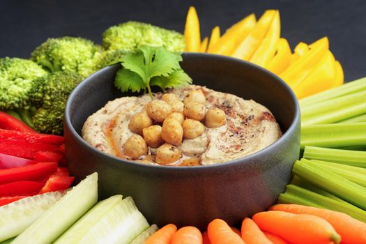 Tasty chickpeas hummus in black plate with fresh vegetables and smoked paprika. High quality photo