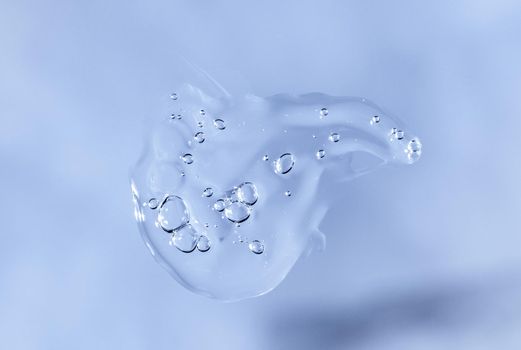 Drop of Fluid hyaluronic acid on blue. Cosmetics and healthcare concept closeup. Dose of serum or retinol with air bubbles. Flat lay. Luxury gel or beauty product presentation in macro