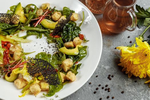 Avocado salad with baby spinach and pomegranate on a black plate on a slate,stone or concrete background.Top view with copy space.