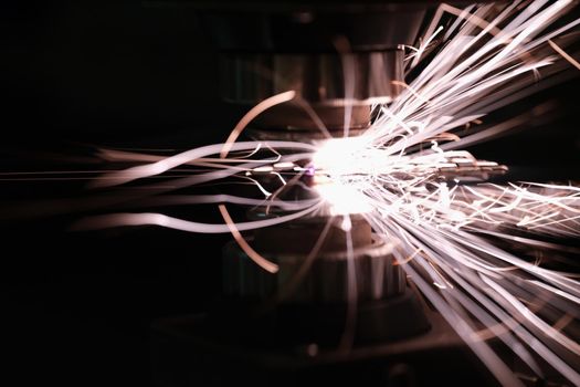 Sparks from metal contact on a machine tool on a dark background, close-up. Iron cutting, metallurgical process, manufacturing
