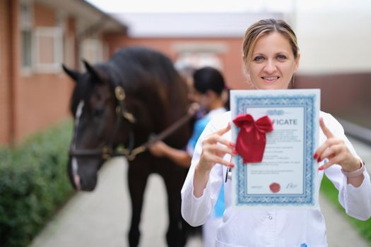 Happy woman vet doctor holding a horse certificate, close-up. Veterinary check-up in the stable. Equine Assisted Therapy