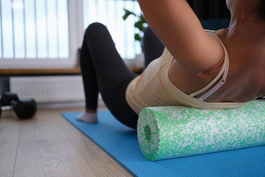 A woman lies on a sports roller, does exercises for the back at home, close-up. Fitness during quarantine