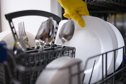 A hand in a yellow glove pulls clean dishes out of the dishwasher. Household appliances for home, kitchen utensils
