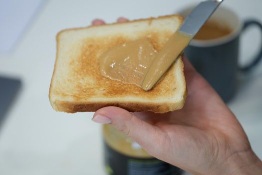 A hand smears peanut butter on a crispy toast made from bread. Traditional homemade American breakfast, unhealthy snack