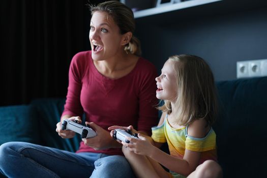 Little girl in the room with her mother playing video games, close-up. Gambling child's game, playstation