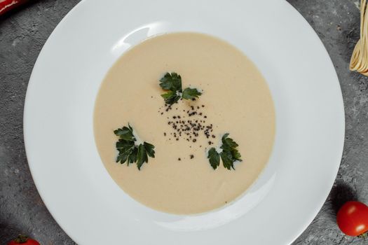 Cheese cream soup with sliced cheese and bread crumbs on a grey background.