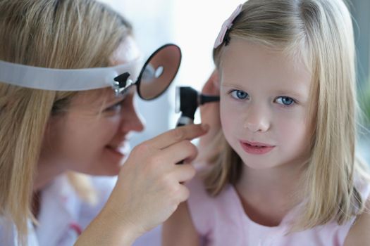 Cute little girl lets the doctor check the woman's ear, close-up, blurry. Pediatrician smiling while examining a child