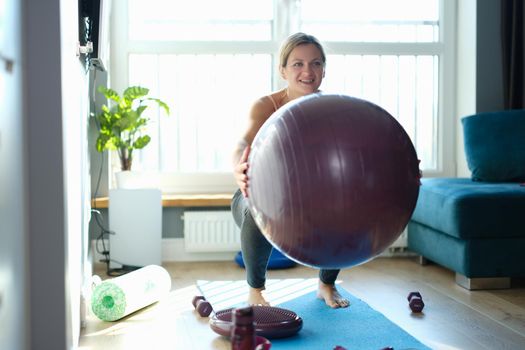 Woman doing squats with a ball at home, sunny, close-up. Fitball training. Strengthening the muscles of the abdomen and lower back