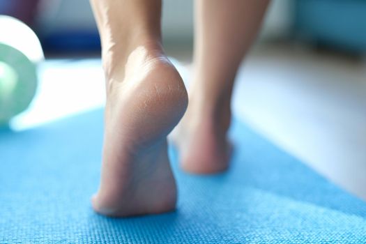 Barefoot dry feet make a step on a sports mat, rear view, close-up. Rough skin of the feet, cracked heels