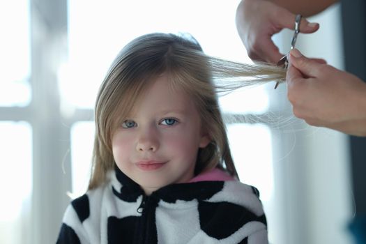 A little cute girl is cutting a lock of hair, close-up. Haircut at home during a pandemic. Children's stylist, hairdressing services