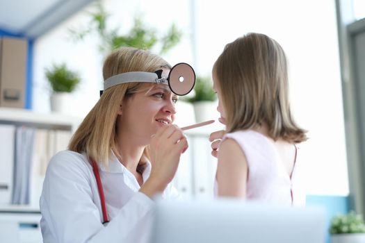 The pediatrician looks at the throat of a little girl, close-up. Visit to otolaryngologist, sick child. Family medicine