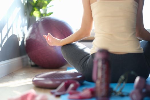 A woman after a workout sits on the floor in a yoga pose, view from the back, sunny. Meditation after sports activities, fitness at home