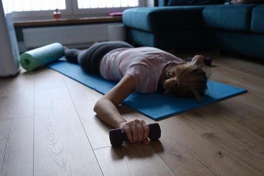 A woman exhausted by sports with dumbbells in her hands lies on the floor, close-up. Physical fatigue after fitness, muscle soreness