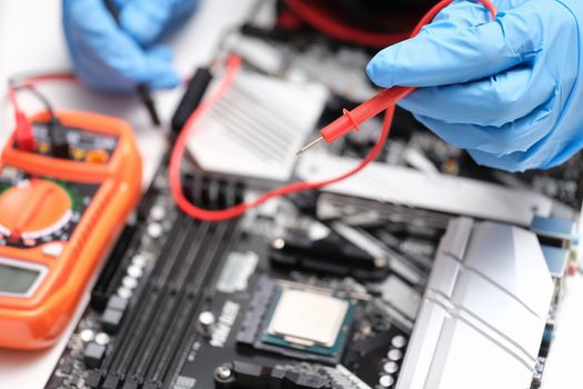 Hands in blue gloves to check electronic equipment with a multimeter, close-up. Repair, electrical troubleshooting, short circuit