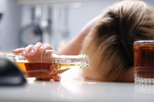 A drunk woman sleeping at the table dropped a bottle of alcohol, close-up. Female alcoholism, a problem in the family