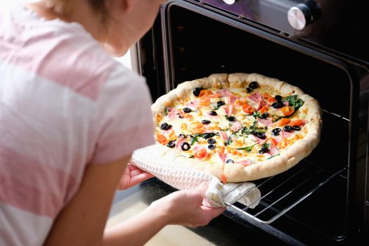 A woman takes out a round homemade pizza from the oven, close-up. Home kitchen appliances for cooking