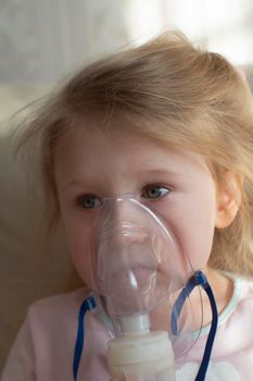 Little girl having inhalation for easing cough. Caucasian blonde girl inhales couples containing medication to stop coughing. Medical procedures. Inhaler. Respiratory medicine.