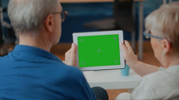 Old couple looking at green screen template on digital device, analyzing blank copy space and isolated chroma key with mock up background. Retired people using modern technology on display.