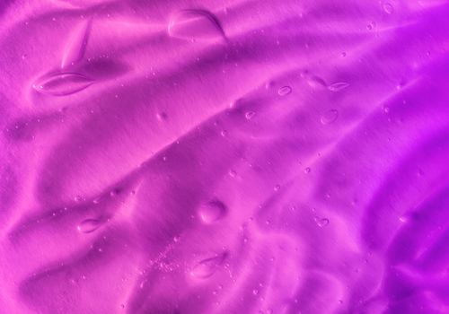Texture of transparent violet gel with air bubbles and waves on orange background. Concept of skin moisturizing, body care and prevention of covid19. Liquid beauty product closeup. Backdrop, flat lay