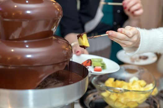 Vibrant chocolate fountain on wedding party. Chocolate fondue with fruits.