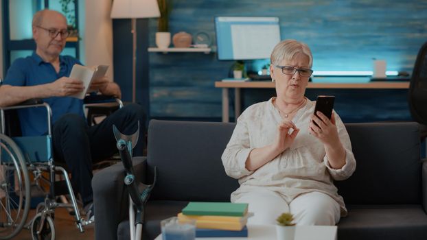 Senior person holding smartphone to talk on teleconference call at home. Retired adult using online videoconference on mobile phone to have remote conversation. Internet telecommunication