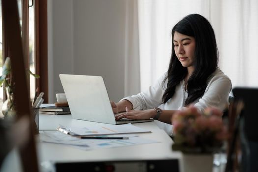 Attractive asian businesswoman sitting on her workplace in the office. Young woman working for financial document data charts with laptop in the office