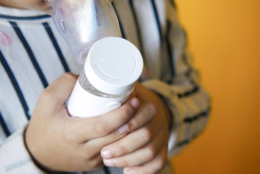 child hand hold a nebulizer against yellow background .