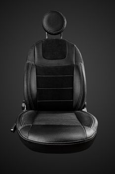 Comfortable driver car seat with round headrest in faux leather with suede inserts isolated on black background, front view