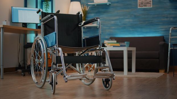 Empty wheelchair in living room to help with mobility and transportation. Nobody in space with walking support equipment to give aid to person with physical disability. Accessibility object