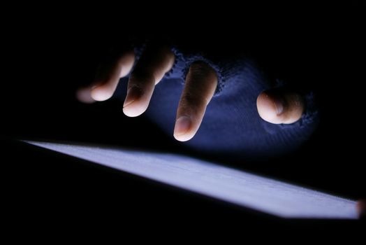 Close up of hacker hand stealing data from digital tablet.