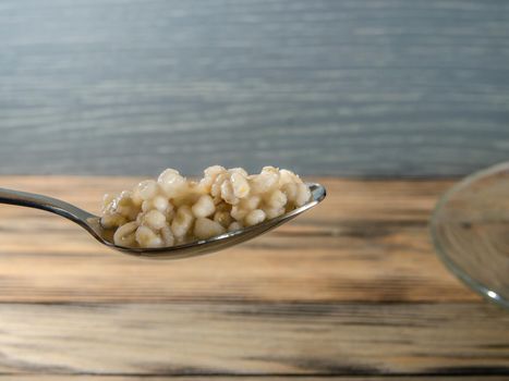 Hot pearl barley porridge in a spoon on a wooden background close-up