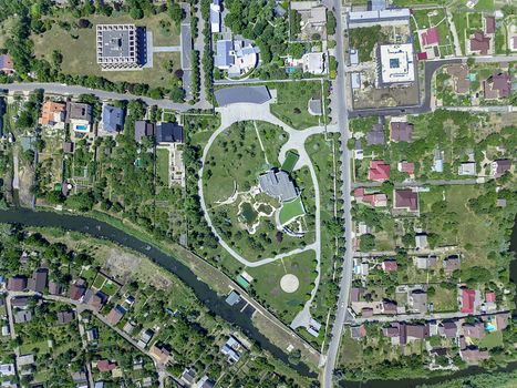 Aerial view of suburban area with private residential buildings surrounded by green lawns and gardens on banks of small river in summer day