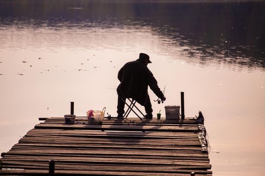 silhouette of a fisherman from behind sitting on a wooden pier during evening fishing.