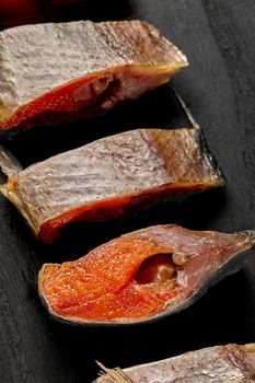 Closeup of slices of salted air-dried roach with roe on black wooden surface. Delicious fish snack