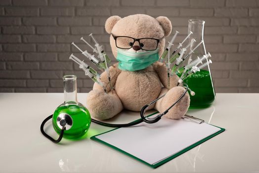 a teddy bear in a medical mask with syringes in his shoulder as a symbol of the research of vaccines and other drugs on animals or people