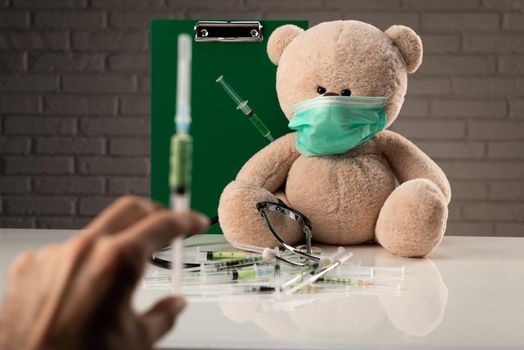 teddy bear in a medical mask with syringes in his shoulder , on the doctor 's desk