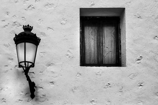 Old house facade with vintage streetlight next to window in Polop village, Valencia community, Spain.