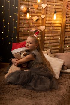 A girl hugs a bear toy in a Christmas cap bear Christmas kid girl happy, for people smiling in lovely sitting room, small baby. Bedroom bed holding, hug wake
