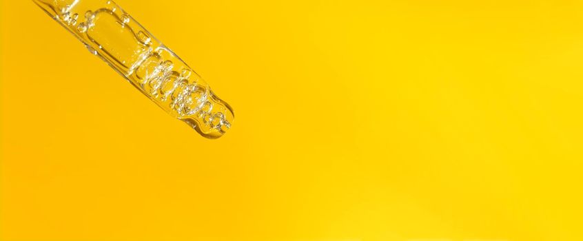Banner of pipette with hyaluronic acid on yellow background. Cosmetics and healthcare concept closeup. Dose of serum or retinol with air bubbles. Flat lay. Luxury beauty product presentation in macro