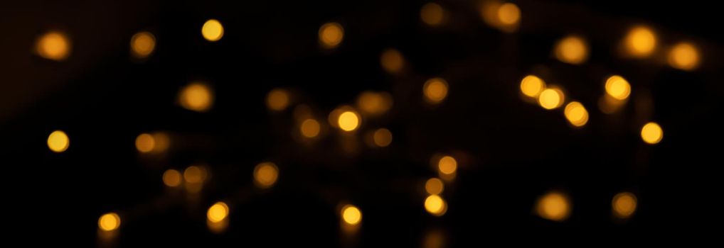 Banner of Defocused bokeh lights on black background, an abstract naturally blurred backdrop for Valentine Day or birthday party. Festive light texture. Yellow, orange garland in blur. Overlay effect