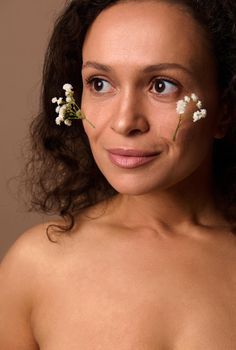 Close-up. Beautiful woman with vitiligo and dermatological skin problems posing with Gypsophila white sprigs on her face. Cosmetology, dermatology, body positivity, skin care concept. Beige background