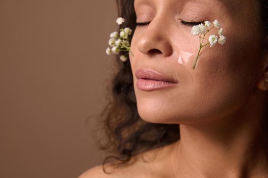 Close-up beautiful woman's face with Gypsophila white sprig on cheeks. Spring, femininity, sensuality, natural beauty people and Women's Day concept on beige background with copy ad space