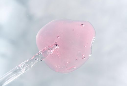 Pipette with pink fluid hyaluronic acid on gray background. Cosmetics and healthcare concept. Dose of serum or retinol with air bubbles. Flatlay. Luxury gel or beauty product presentation in macro