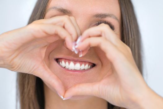 Teeth care. Woman with beautiful smile with strong white teeth. Dental care. Woman holding heart shaped hands near perfect healthy teeth. Stomatology or dentistry concept. High quality photo