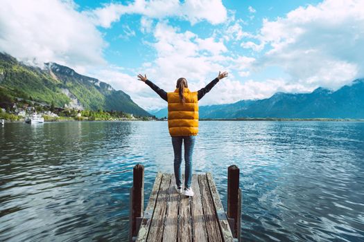 Young woman traveler with open arms standing on wooden bridge and enjoying great view on Geneva lake in Switzerland. High quality photo