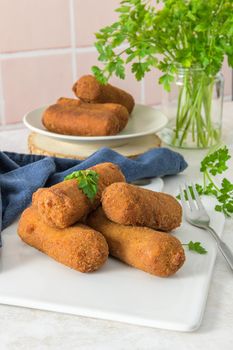 Meat croquets and parsley leaves on white ceramic dishes in a kitchen counter top.