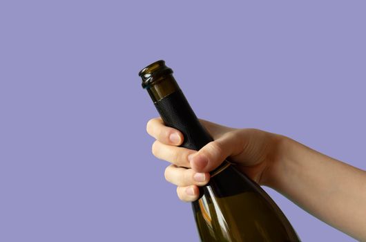 A woman's hand holding an open bottle of champagne on a lilac background. Very peri.