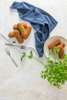 Meat croquets and parsley leaves on white ceramic dishes in a kitchen counter top.