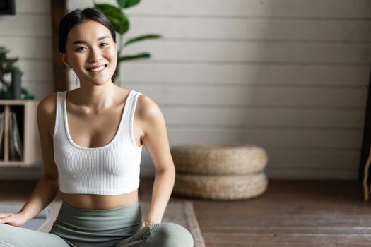 Mindfulness and meditation concept. Young asian woman doing workout at home, yoga meditation in living room on floor mat, getting focused.